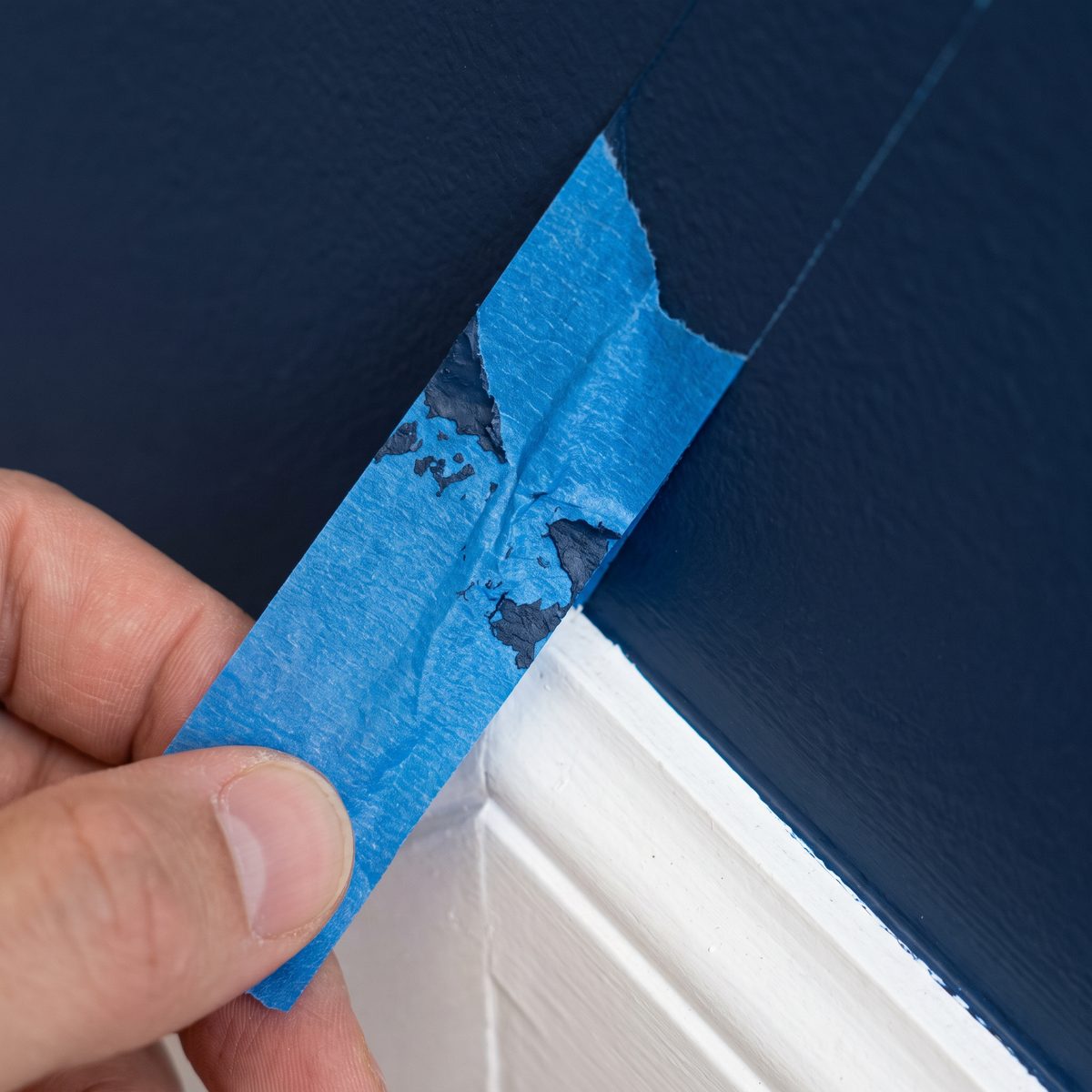 Painter's tape peeled back to show a sharp edge between a navy wall and white trim, concept imagery